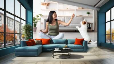 Cheerful asian woman playing with dog while exercising at home Wall mural