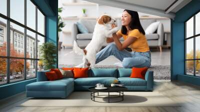 Cheerful asian woman training her dog, giving treats Wall mural