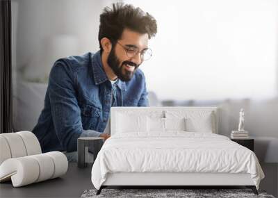 Cheerful bearded indian man looking at his smartphone with smile at home Wall mural