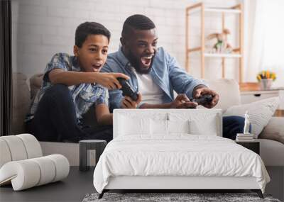 Cheerful Black Father And Son Competing In Video Games At Home Wall mural