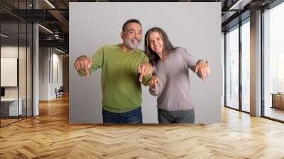 Cheerful caucasian senior man and lady pointing fingers down at copy space recommending ad and offer Wall mural