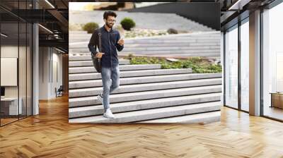 Cheerful indian guy going down stairs outdoors, using cell phone Wall mural