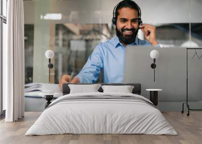 Cheerful indian man with headset working online on laptop Wall mural