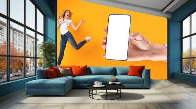 Cheerful lady jumping and pointing at empty smart phone screen Wall mural