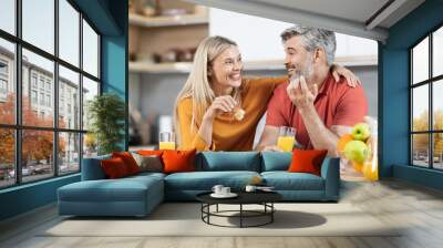 Cheerful man and woman having snack and talking at home Wall mural