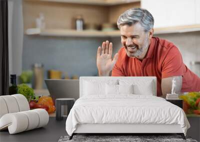 Cheerful man cooking at home, having video call, using laptop Wall mural