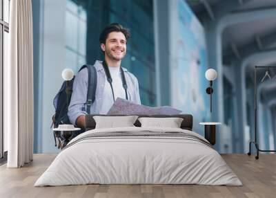 Cheerful man traveler holding map, studying new destinations at airport Wall mural