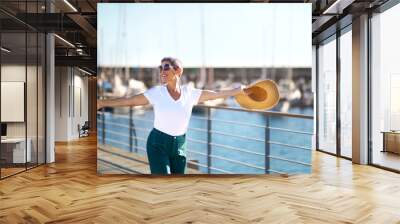 Cheerful Mature Woman Posing Holding Hat At Marina Dock Outdoor Wall mural