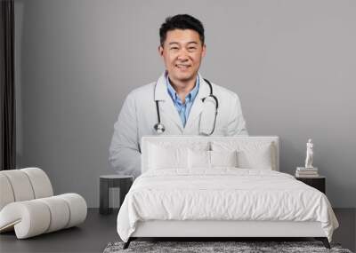 Cheerful middle aged asian male doctor in white coat with stethoscope, tablet isolated on gray background Wall mural