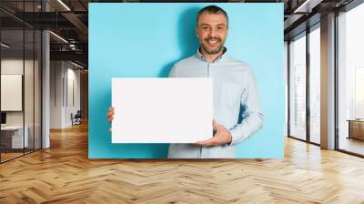 Cheerful Middle Aged Male Holding Blank Paper Poster, Blue Background Wall mural