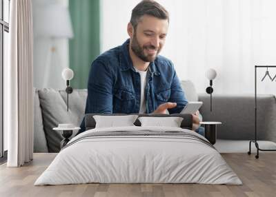 Cheerful middle-aged man sitting on sofa with mobile phone Wall mural