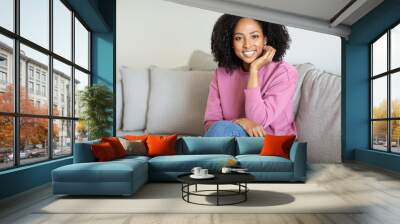 Cheerful millennial black woman relaxing, enjoy free time, weekend, sit on sofa in minimalist living room interior Wall mural