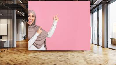 Cheerful muslim woman pointing at copy space on pink background Wall mural