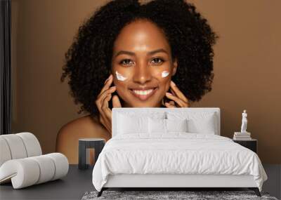 Cheerful pretty young black woman applying cream on face Wall mural