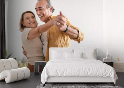 Cheerful retired spouses husband and wife dancing and laughing in living room, happy romantic couple enjoying slow dance Wall mural