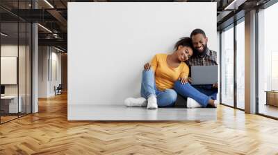 Cheerful young black man and woman look in laptop, planning interior, sits on floor in empty room Wall mural