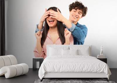 Cheerful young boyfriend surprising girlfriend covering eyes over white background Wall mural