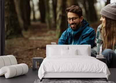 Cheerful young caucasian family in jackets relaxing, drink coffee, look at route map on smartphone Wall mural