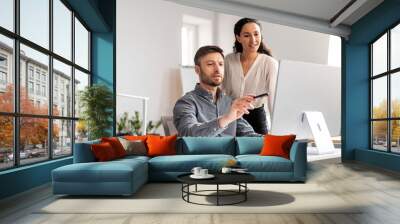 Cheerful young caucasian male manager show to lady with hand at computer in modern office interior Wall mural