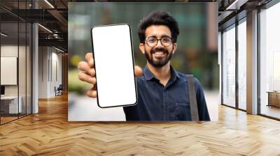 Cheerful young indian guy showing smartphone with white blank screen Wall mural