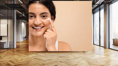 Cheerful young indian woman applying dab of moisturizing cream on her face Wall mural