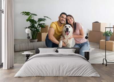 Cheery young international couple with cute golden retriever dog sitting on floor of new home on relocation day Wall mural