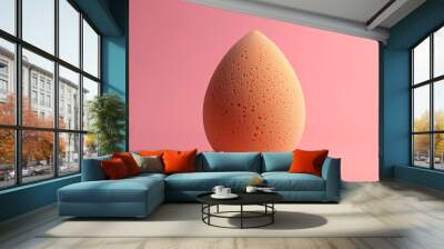 Close-up of a soft, orange beauty blender standing upright on a pink background, captured in studio lighting. Wall mural