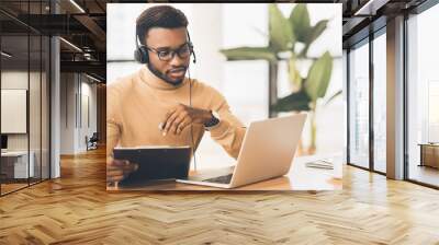 Concentrated consultant with headset looking at laptop Wall mural