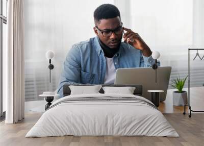 Concerned african american employee talking on mobile phone and looking at laptop screen, having issues with project, copy space Wall mural