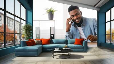 Confident black businessman talking with companion on phone and checking financial reports at workplace in office Wall mural