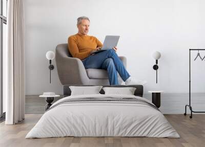 Confident mature man using laptop sitting on chair Wall mural