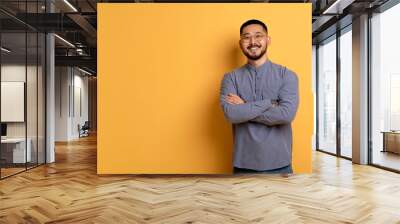 Confident young asian man standing with folded arms over yellow background Wall mural