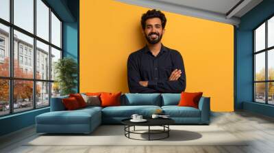 Confident young indian man standing with folded arms over yellow background Wall mural