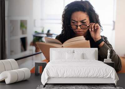 Confused black lady in glasses trying to read book Wall mural