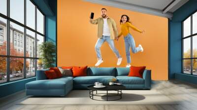 Couple Jumping And Showing Smartphone With Empty Screen, Orange Wall Wall mural