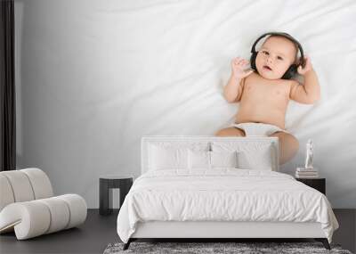 Cute baby with headphones lying on white bed Wall mural