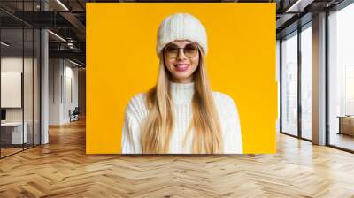 Cute cheerful winter girl in sunglasses smiling over yellow background Wall mural