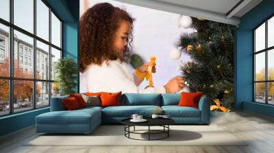 Cute little afro girl decorating Christmas tree at home Wall mural