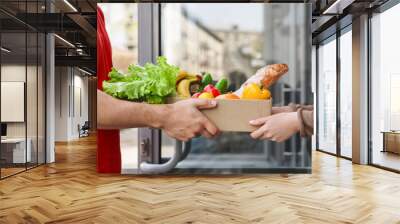 Delivery from supermarket. Courier hands over box of food Wall mural