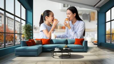 Dessert time for sweet tooth. Happy asian girl and young woman eating cookies, sitting at dinner table in kitchen Wall mural