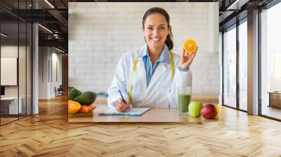 Dietician with orange in kitchen, writing nutrition plan Wall mural