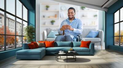 Disabled black man in wheelchair using smartphone, browsing web or watching movie at home Wall mural