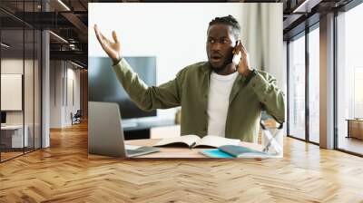 Discontented black man talking on cellphone and using pc, having problem with internet connection at home Wall mural