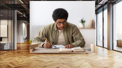 Distance learning. Black teen college student with textbook and copybook studying at home during lockdown Wall mural