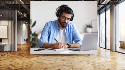 Distance Learning. Young Arab Guy In Headphones Studying With Laptop At Home Wall mural