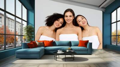 Diverse beauty concpet. Three multiracial ladies wrapped in towels, posing and smiling at camera over grey background Wall mural