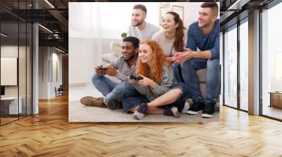 Diverse friends playing video games, sitting on floor at home Wall mural