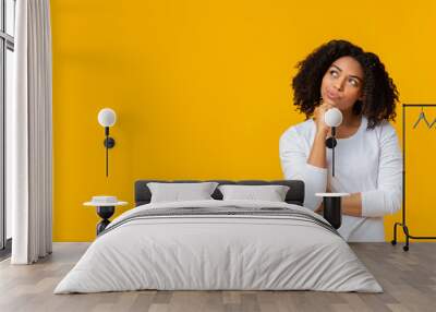 Doubtful afro girl thinking about something over yellow background Wall mural