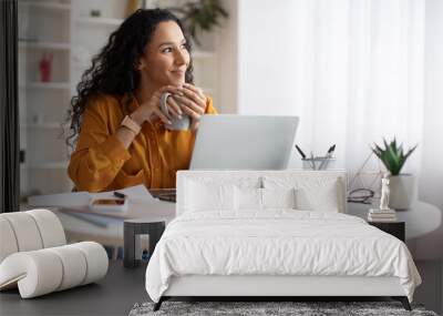 Dreamy Businesswoman Using Laptop And Holding Coffee Cup Indoors Wall mural