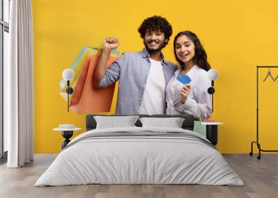 Easy payment. Portrait of indian couple showing debit credit card holding shopper bags after purchases in shopping mall Wall mural